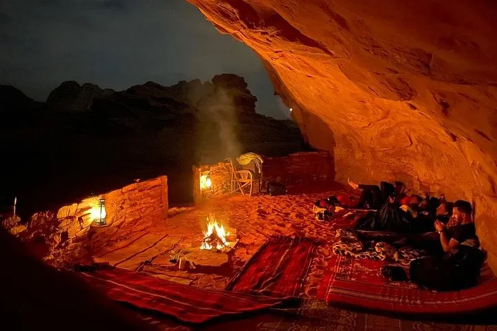 Campers by a fire near a rock cave at dusk on a Wadi Rum desert tour with cave camping