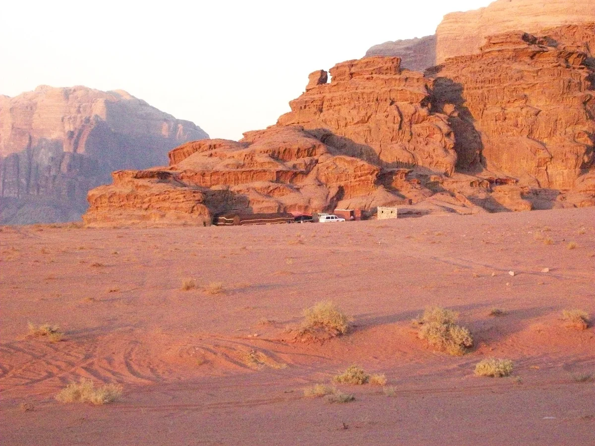 A Bedouin camp below red cliffs at sunset on a Wadi Rum desert tour with an overnight